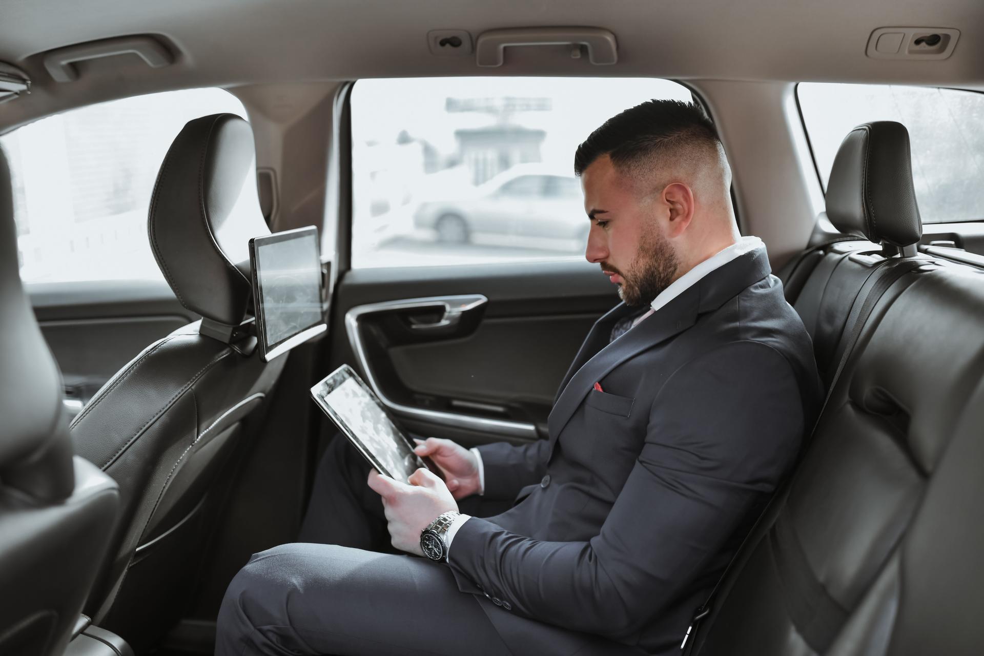 Concentrated Male CEO Examining Reports on Digital Tablet While Sitting in Backseat of Luxurious Car